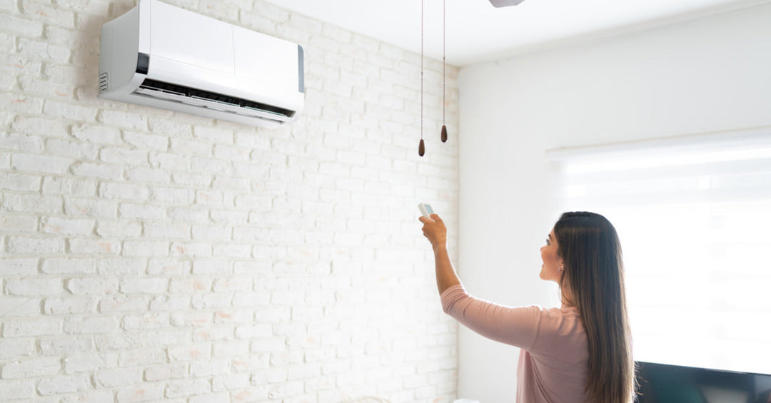 A woman points a remote control toward a wall-mounted mini split system to adjust the temperature in the room.