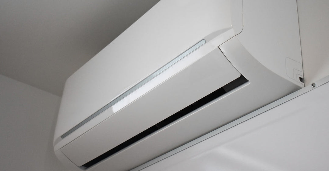 A close-up upward shot of a white mini-split heating and cooling system mounted to a white wall.