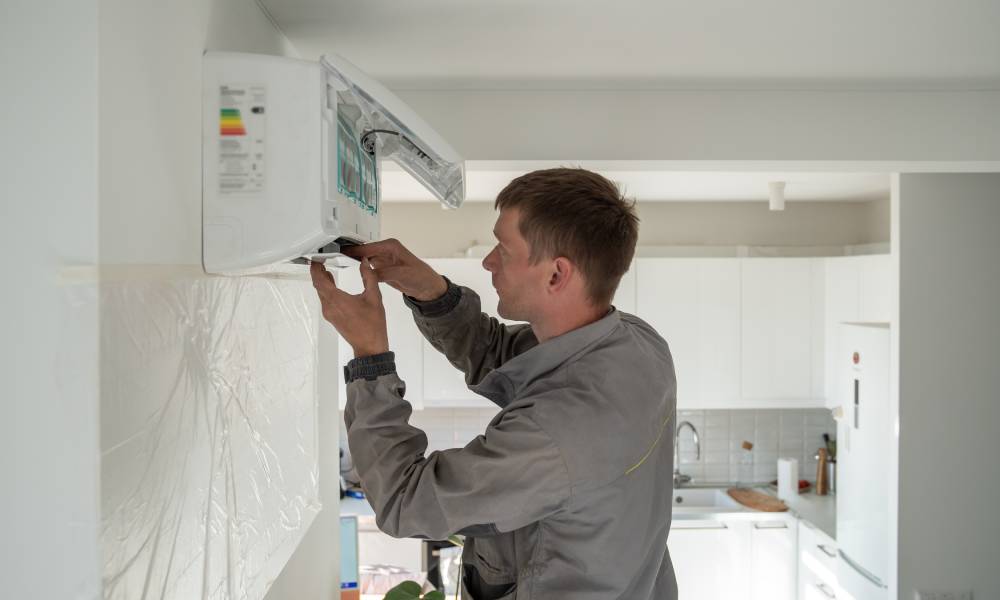 A technician in a grey jacket repairing and maintaining a mini split installed near the ceiling in a client's home.