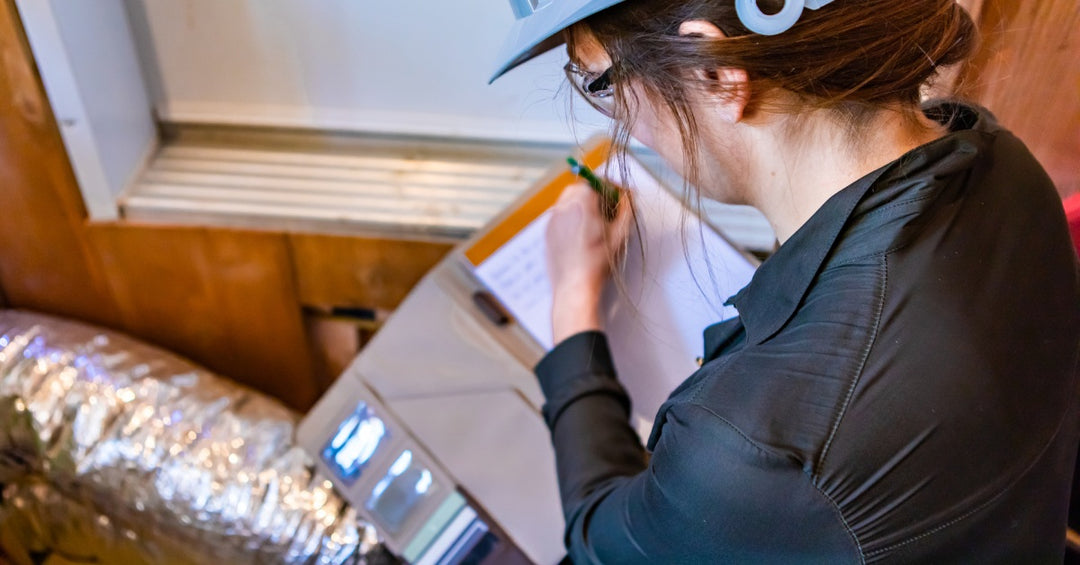 A female energy audit inspector with a clipboard is assessing an aluminum tube and its insulation.